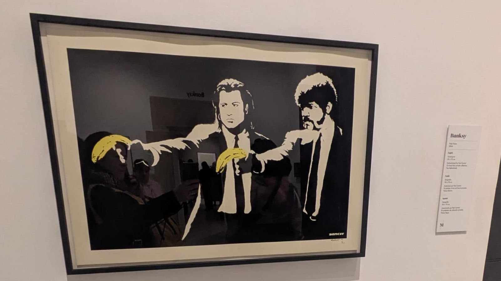 La imagen muestra la famosa obra de arte urbano "Pulp Fiction" del artista Banksy, que parodia la película de Quentin Tarantino reemplazando las armas de los personajes por plátanos.