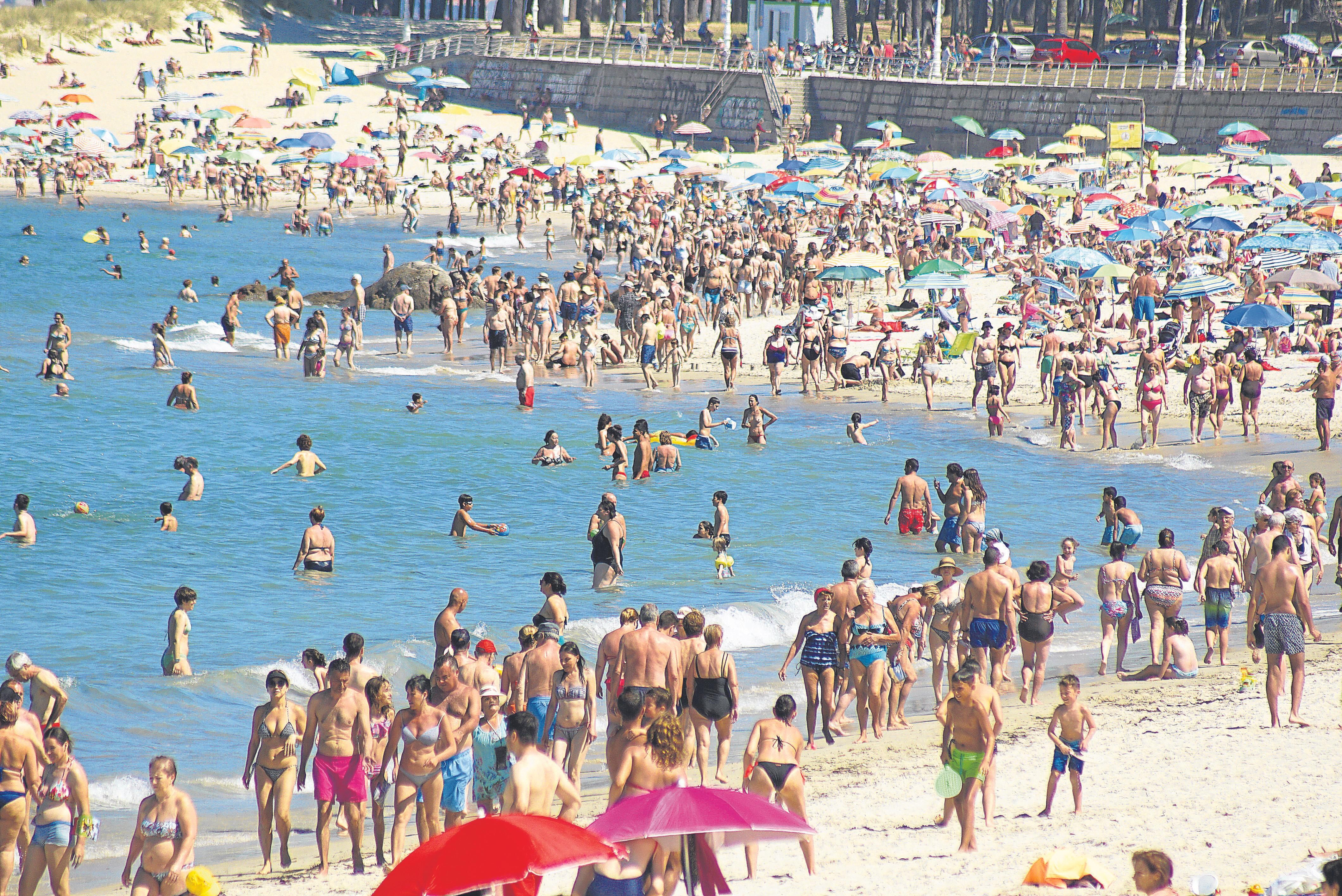 La playa de Samil es la más concurrida de la ciudad. En la fotografía la orilla abarrotada de gente paseando, bañándose y niños jugando en un día de calor de julio.