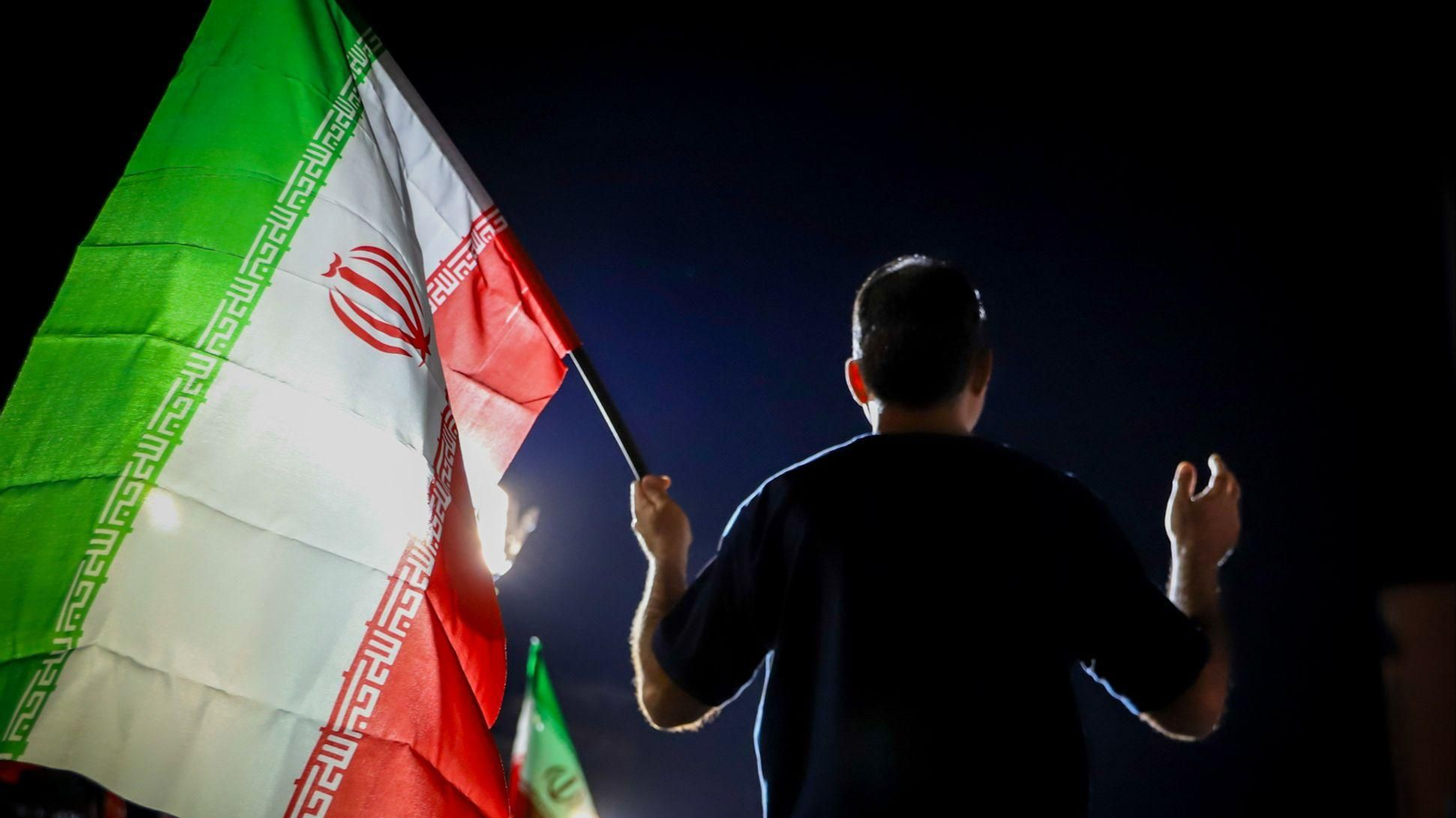 Un partidario progubernamental iraní sostiene una bandera iraní durante una manifestación nocturna en una calle.