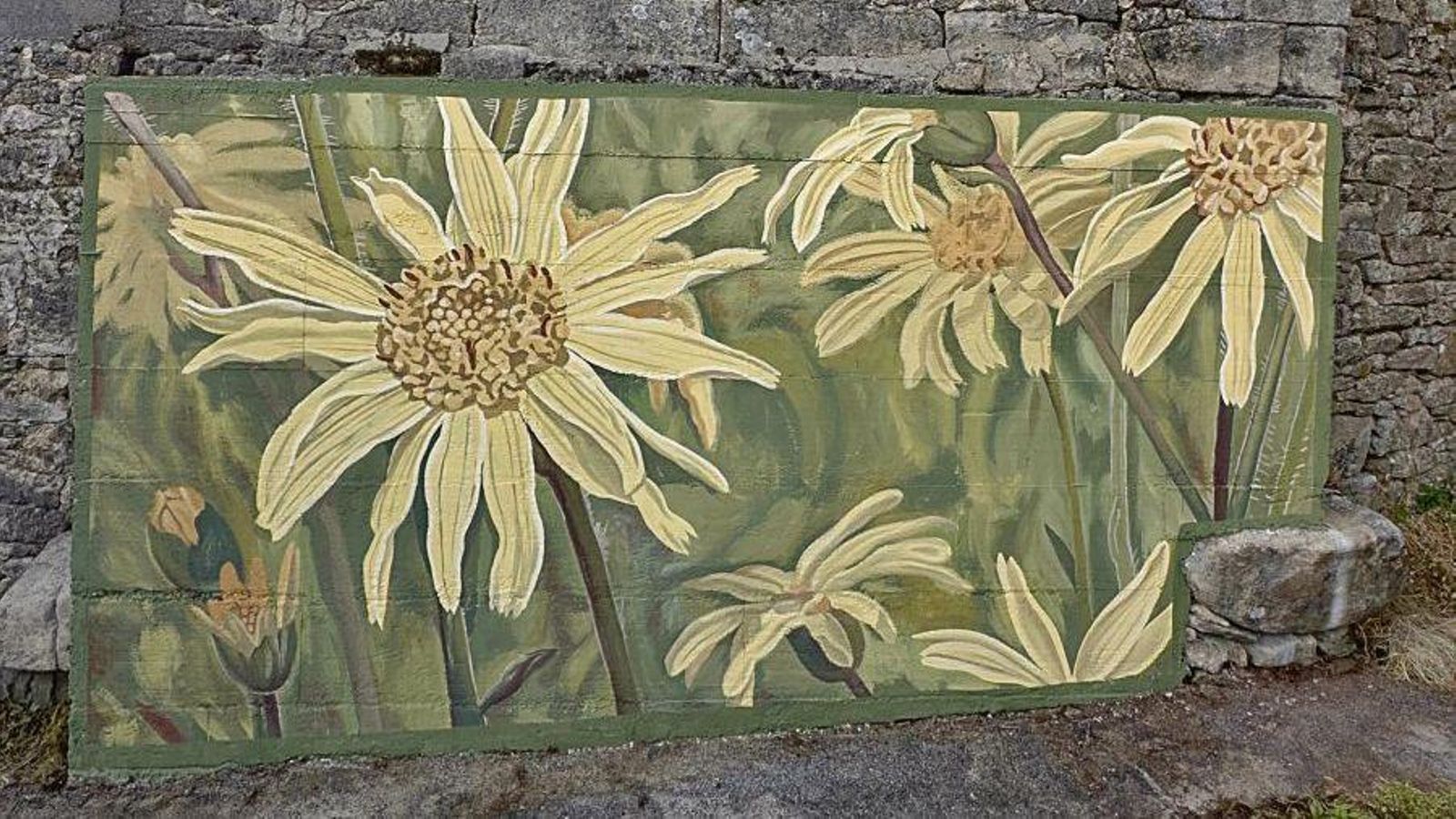 Grandes flores de árnica pintadas en la parte inferior de una fachada de piedra tradicional.