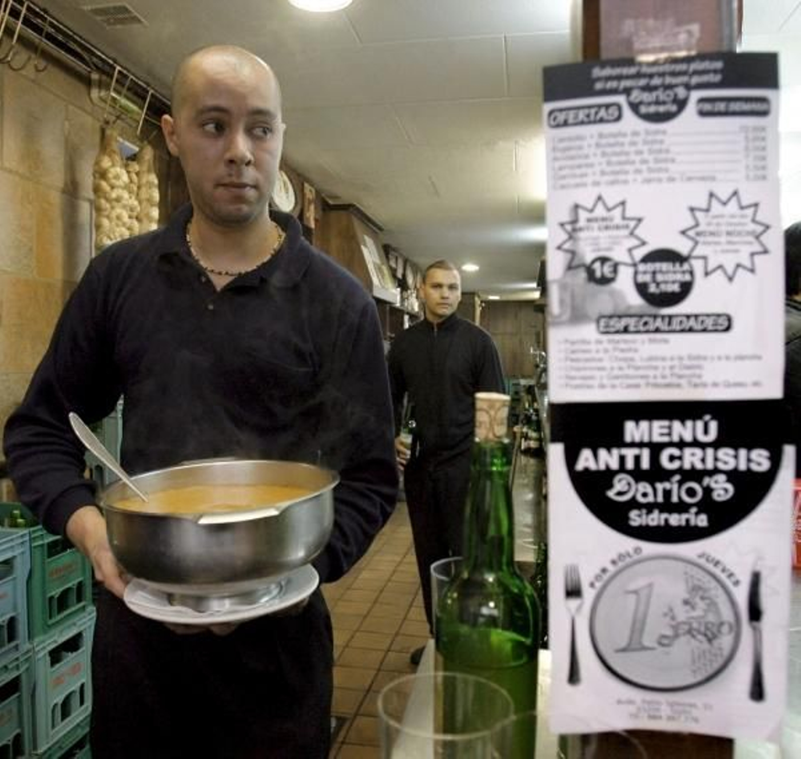 Un camarero de la sidrería, con el cartel que anuncia los menús a un euro. (Foto: Juan González)