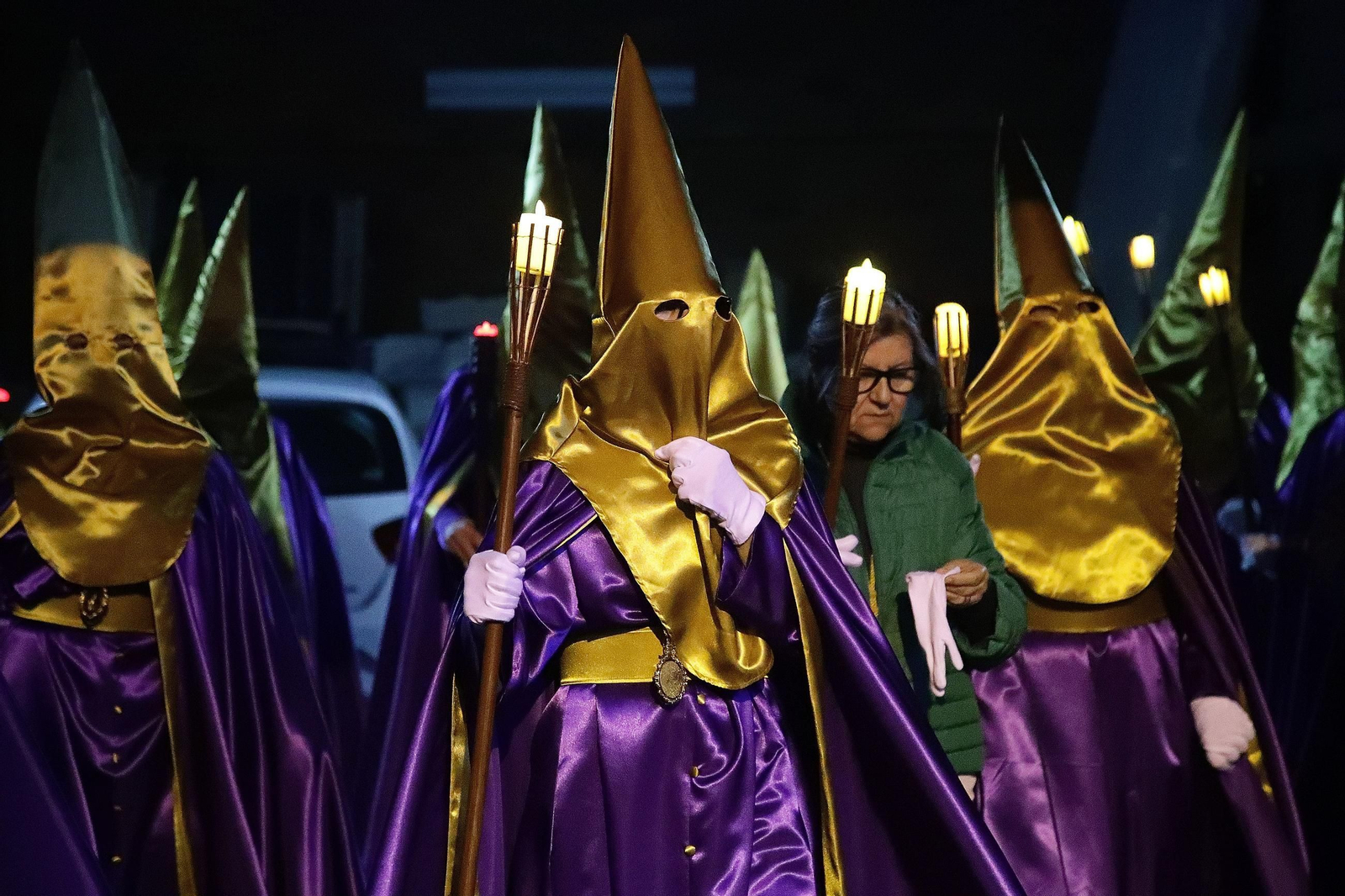 Los cofrades, vestidos de morado y oro, recorren las calles del barrio.