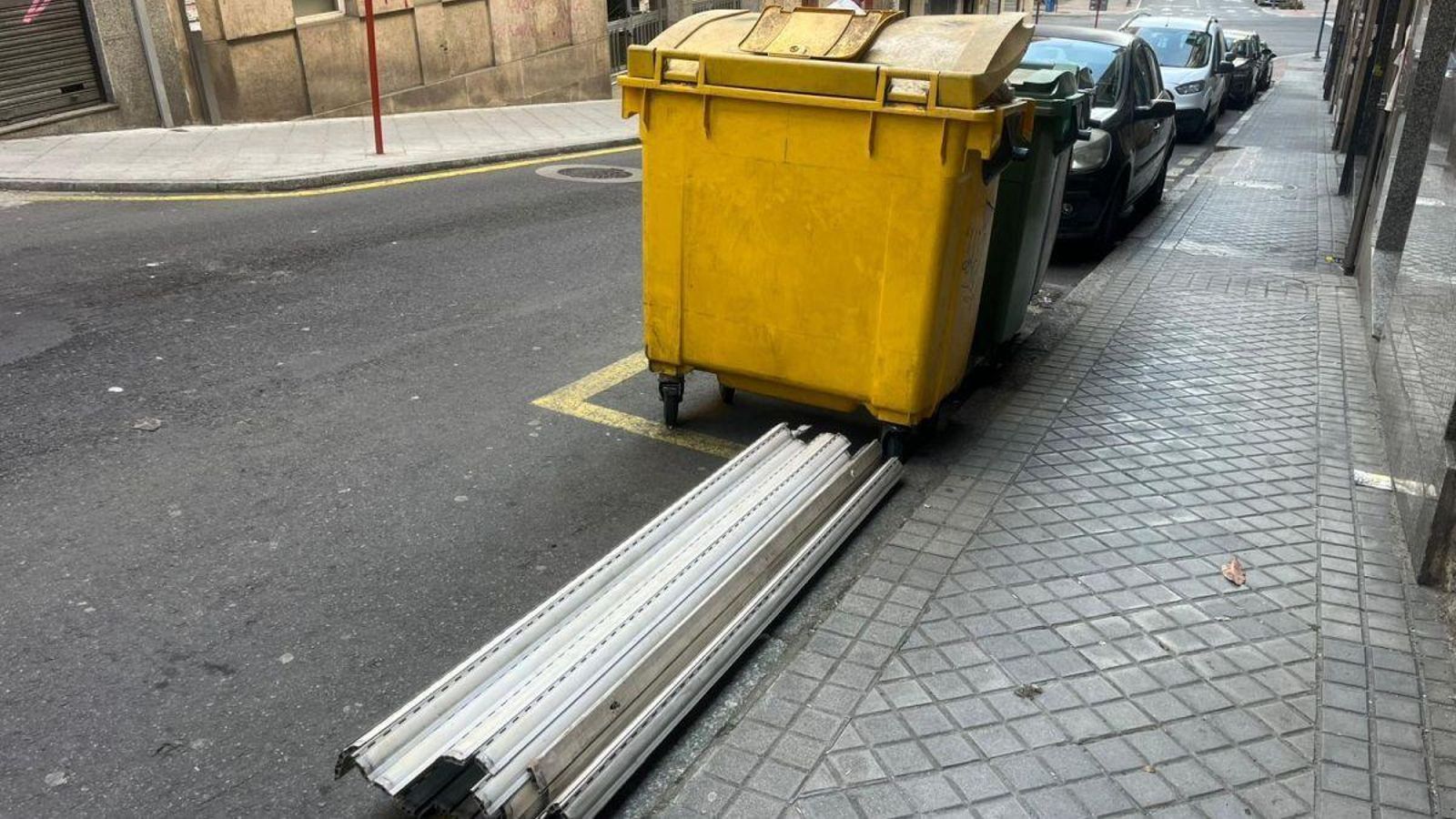 Persianas en la vía pública al lado de un contenedor.