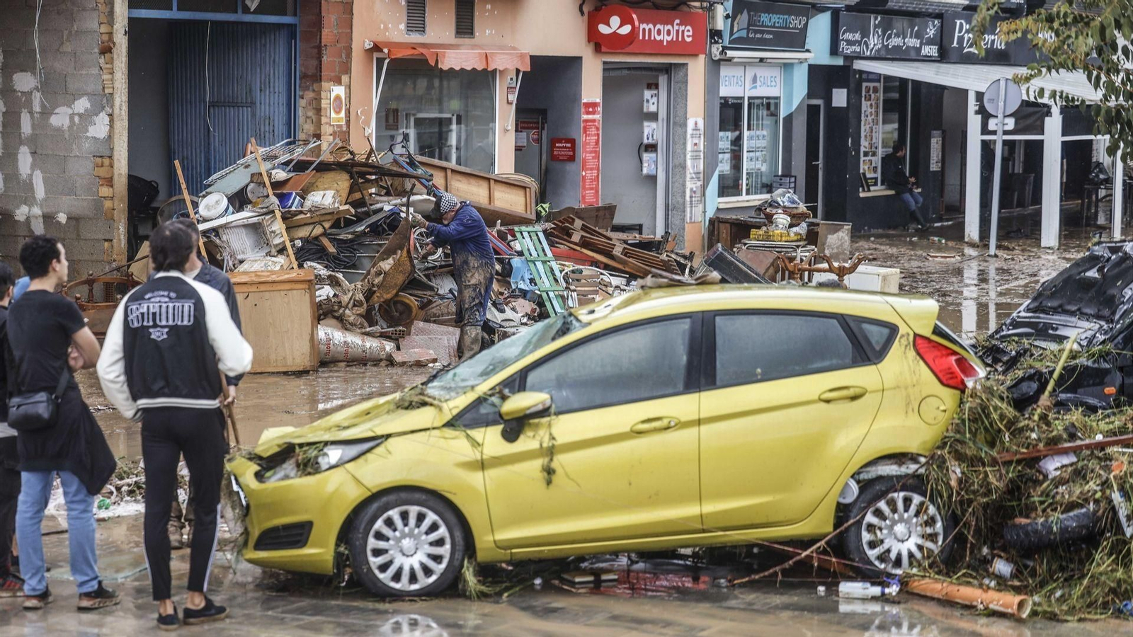 Varias personas quitan el barro de las calles mientras se acumula el mobiliario que han tenido que sacar debido a las inundaciones por las fuertes lluvias, a 19 de octubre de 2026, en Els Poblets, Comunidad Valenciana.