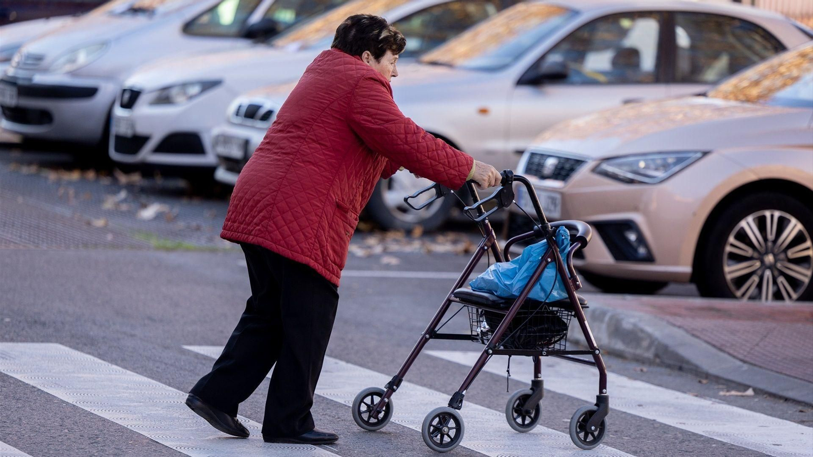 Una mujer mayor camina con un andador y cruza un paso de cebra.