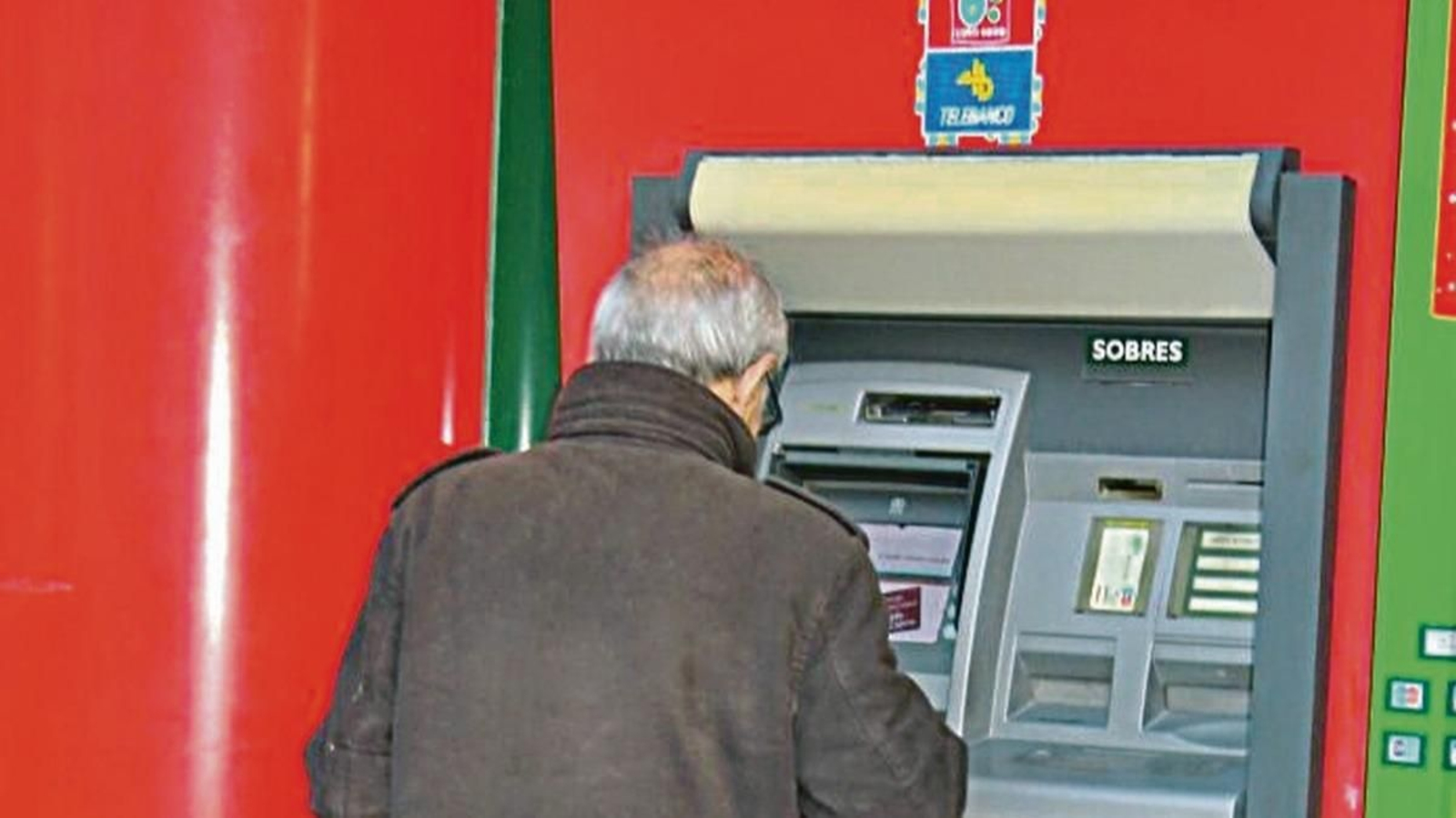 Una persona mayor retira dinero en efectivo con su tarjeta en un cajero automático.