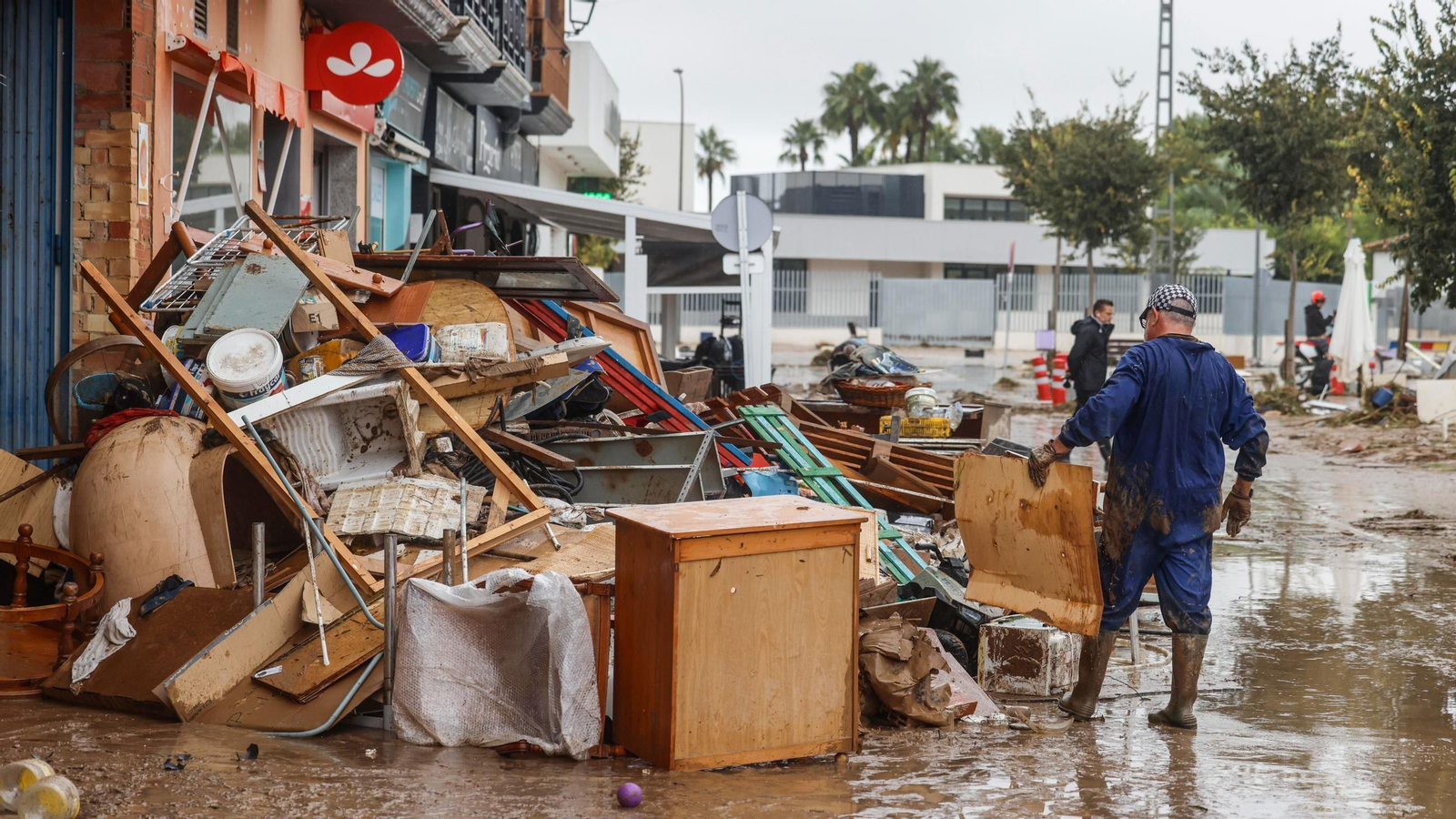 Varias personas quitan el barro de las calles mientras se acumula el mobiliario que han tenido que sacar debido a las inundaciones por las fuertes lluvias, a 19 de octubre de 2026, en Els Poblets, Comunidad Valenciana