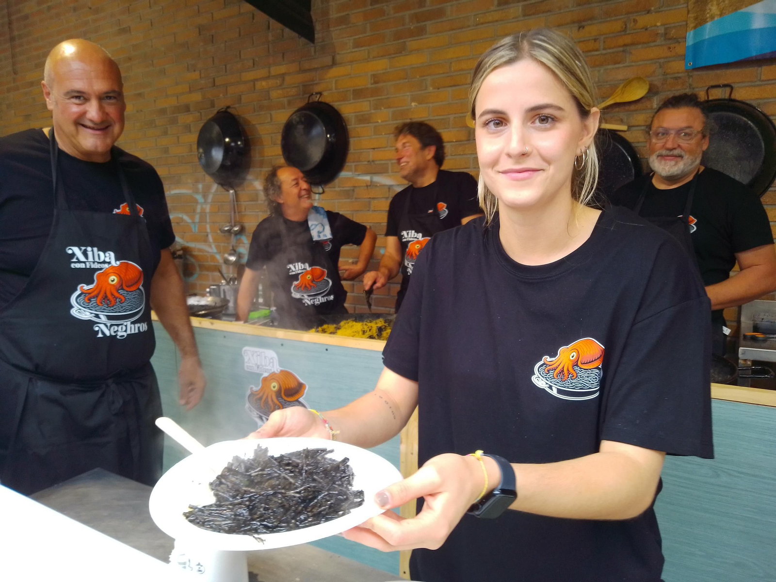 Una de las cocineras muestra la ración de sepia con fideos negros.