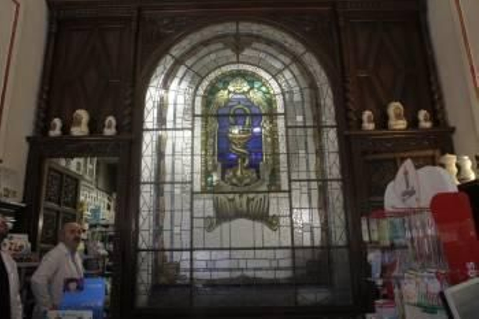 La vidriera principal, en tonos azules y verdes con el logotipo de la profesión, está situada detrás del mostrador, a la vista del público. Las paredes y los muebles de la farmacia son obra de los famosos Hermanos Rodríguez. (Foto: FOTOS MIGUEL ÁNGEL)