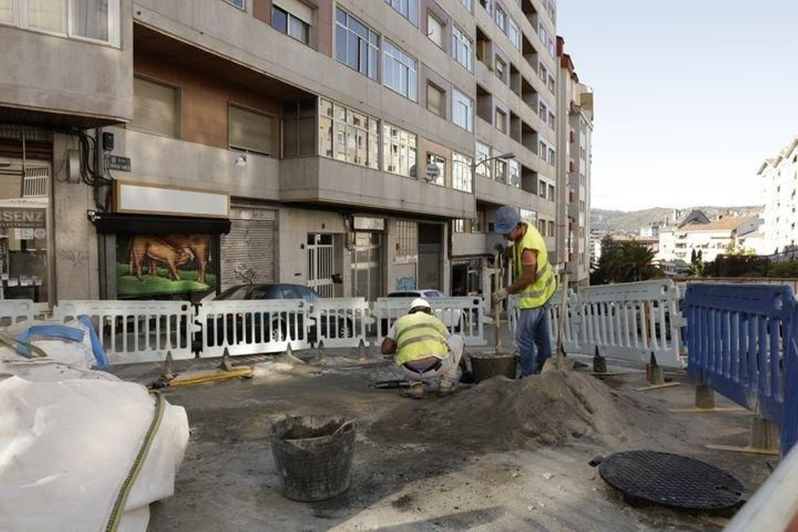 Dos operarios trabajan sobre el firme de la calle, que fue vallado.