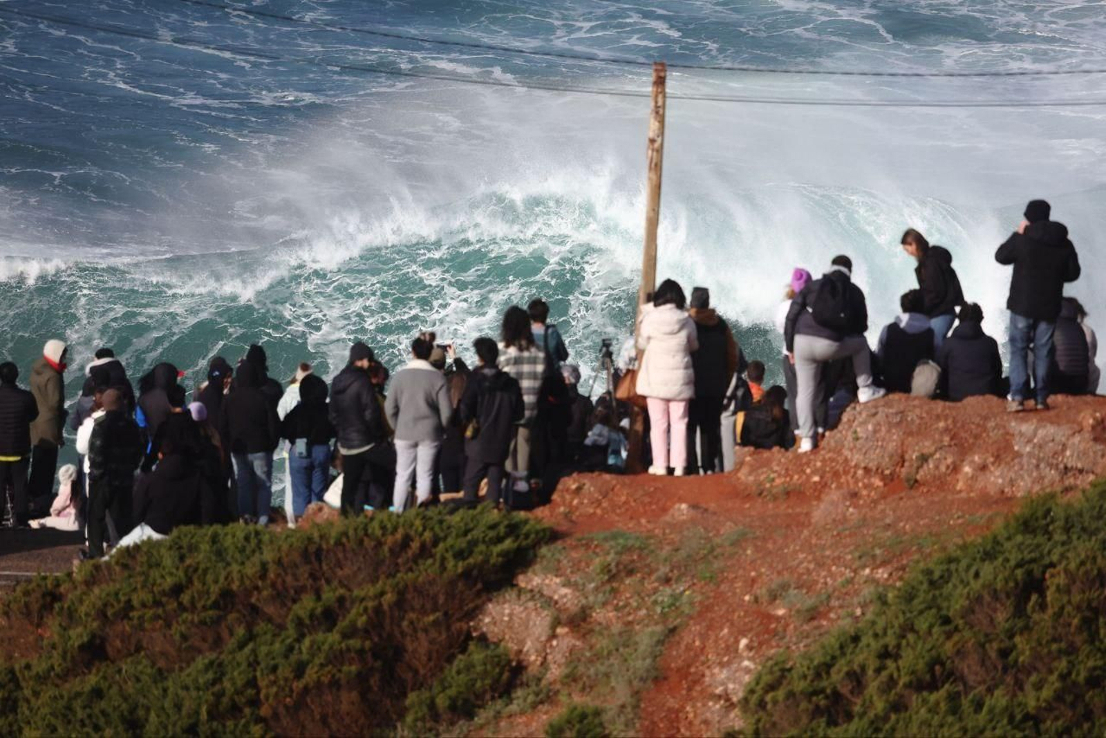 Gente viendo como hacen surf extremo en Nazaré, Portugal.