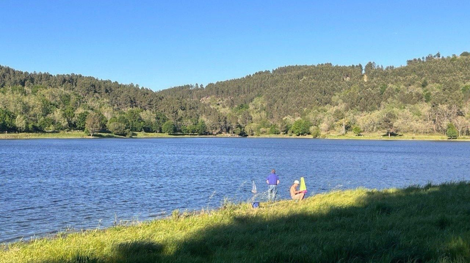 Dos personas disfrutan del buen tiempo con sus barcos teledirigidos en el embalse de Cachamuiña.
