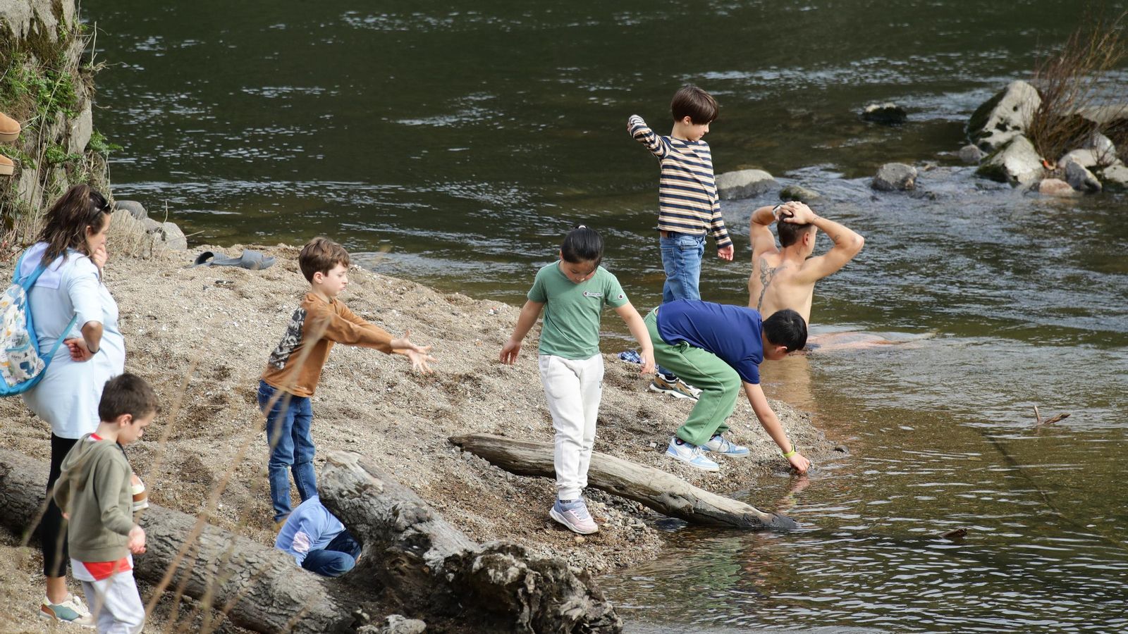 Un hombre en el agua del río refrescándose mientras los niños juegan a la orilla.