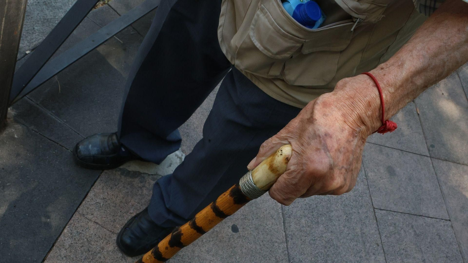 Persona mayor caminando por la calle ayudada por un bastón