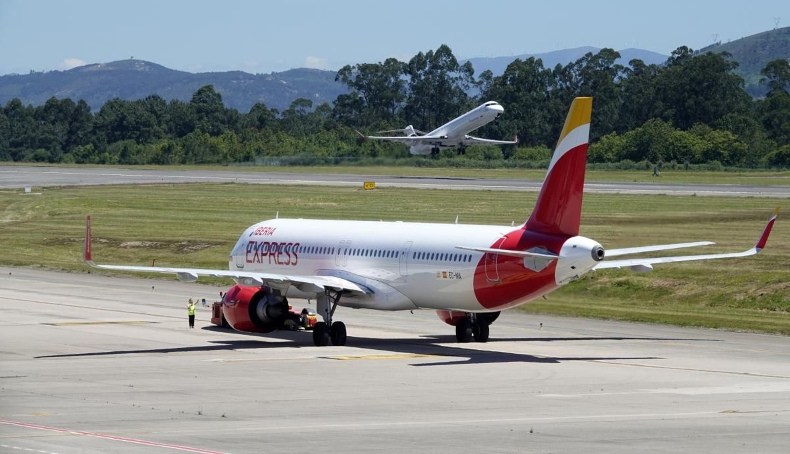 Un avión de la compañía Iberia Express se mantiene estacionado mientras otro despega en la pista de Peinador.