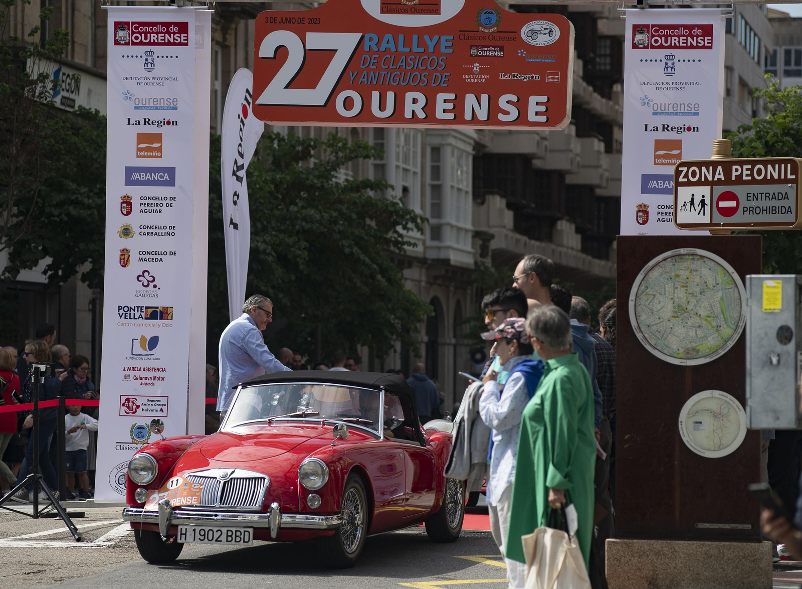 Grupo de gente observando un coche de rally clásico circulando por la calle del paseo en Ourense