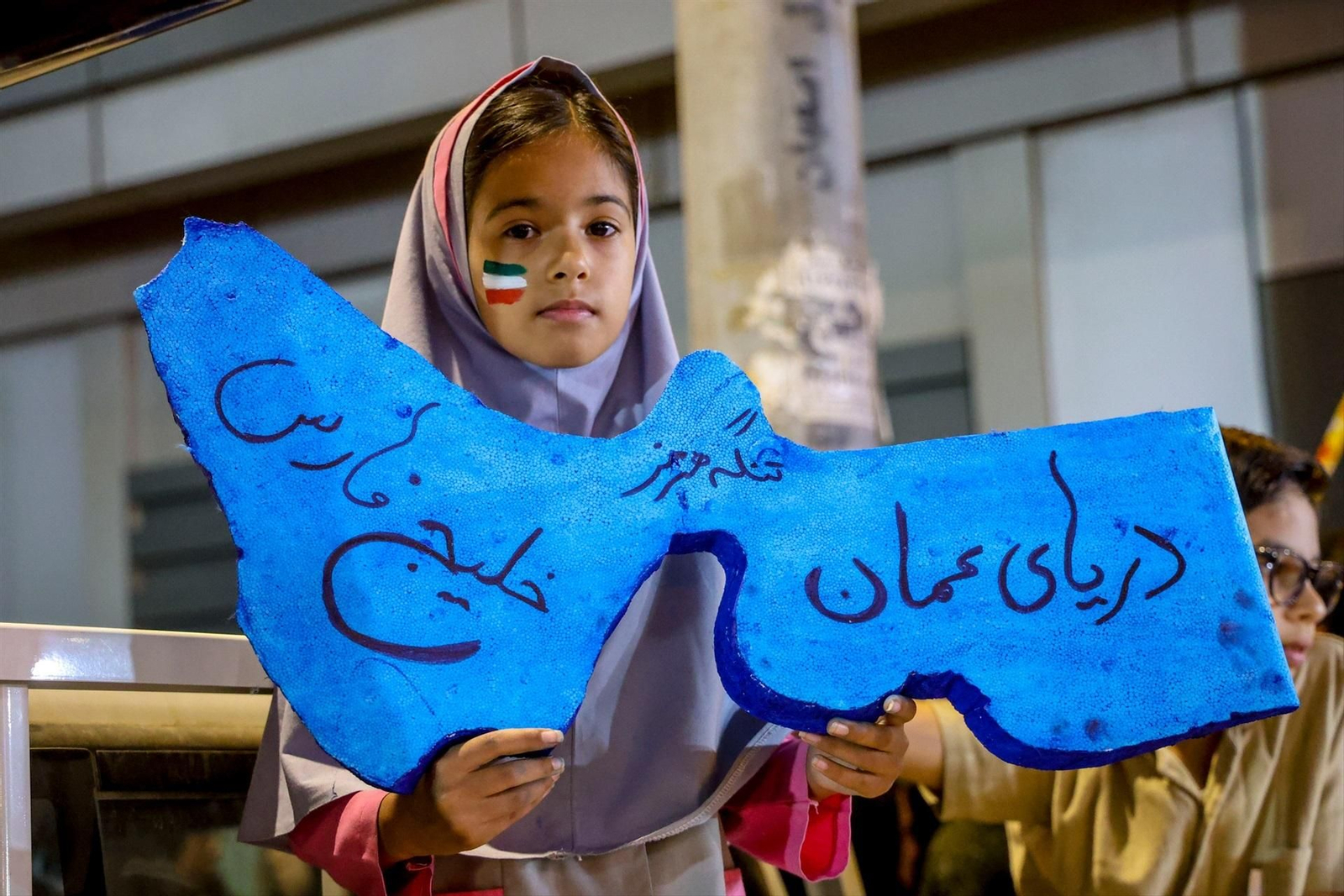 Una niña iraní en una protesta, con una recreación del estrecho de Ormuz en las manos