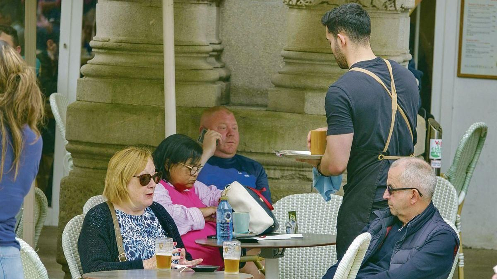 Un camarero atiende a unos clientes en la terraza de un local de restauración de Vigo.
