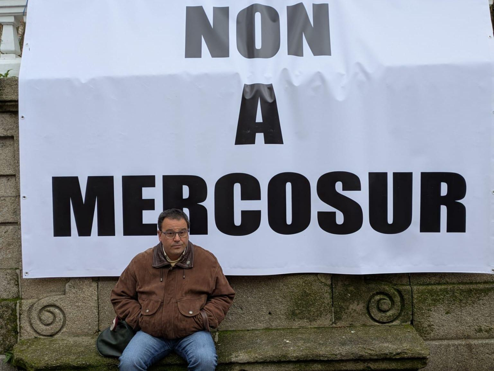 Un señor junto con el cartel de protesta