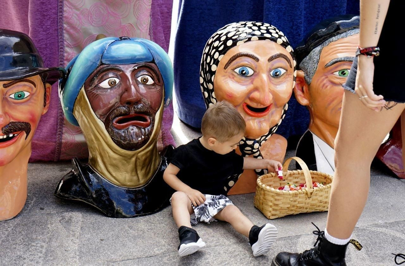 Un niño sentado entre las cabezas de  los cabezudos.