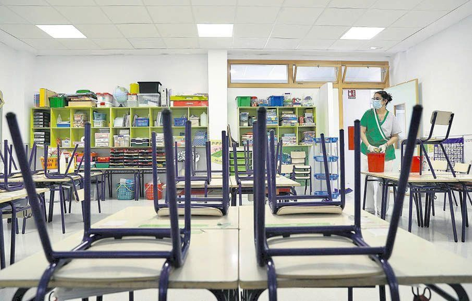 Una trabajadora del servicio de limpieza desinfecta los pupitres de un aula de infantil.