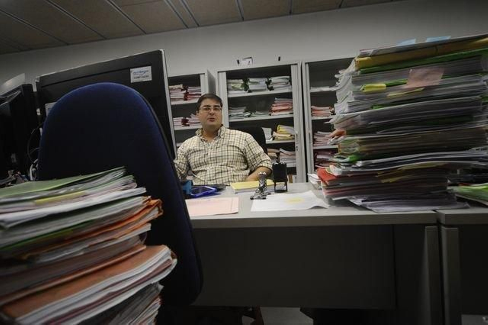 El gestor Alberto Fernández Rey mira a cámara sentado en su lugar de trabajo en el  Juzgado de Familia de Ourense (Instancia 6). A su alrededor, pilas de asuntos. (MARTIÑO PINAL)