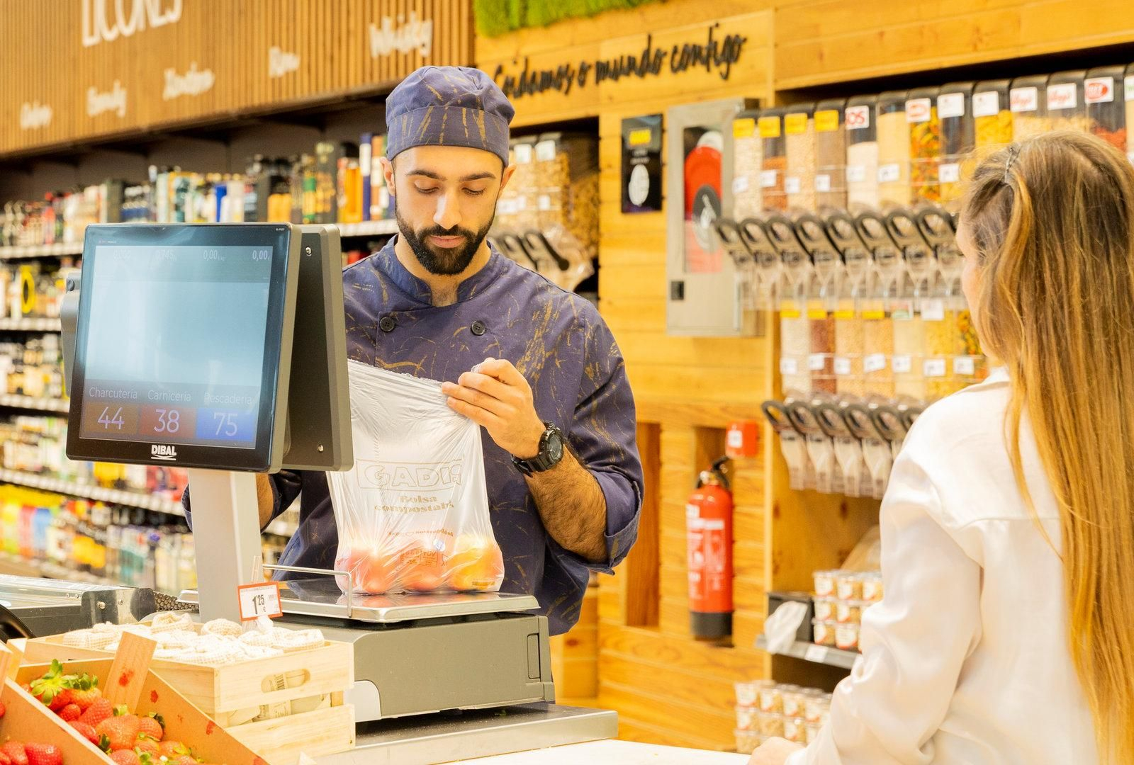 Un empleado atiende en la frutería de un supermercado Gadis a una clienta.