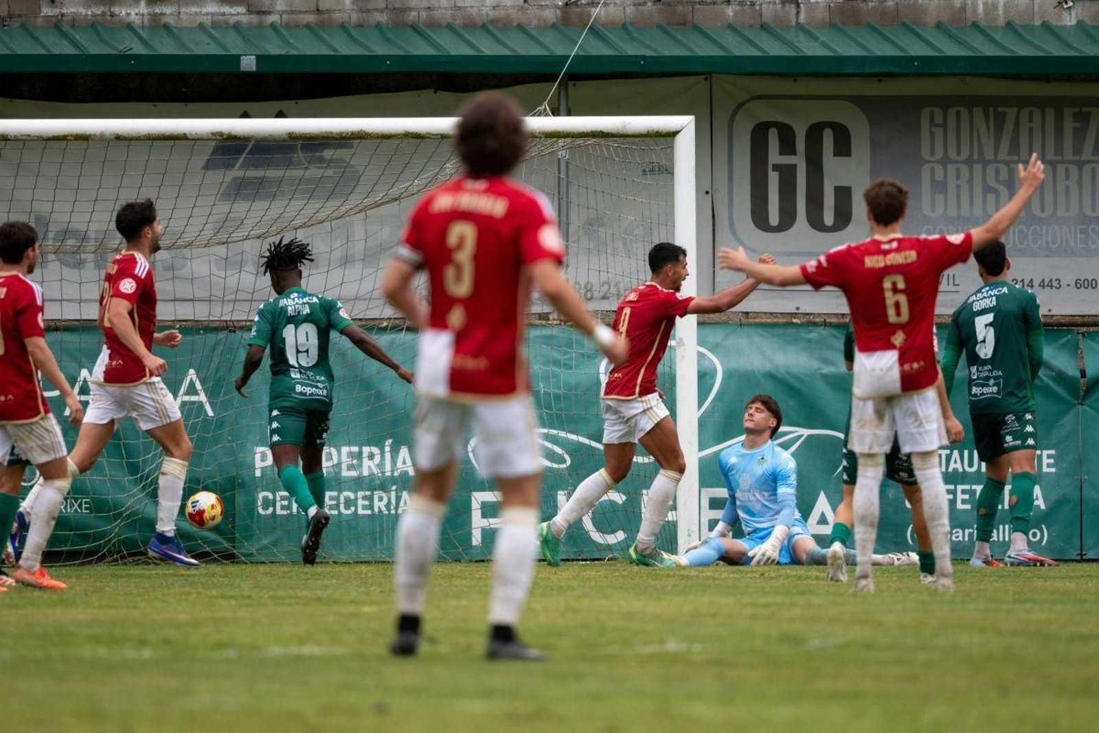 Los jugadores del Arenteiro se lamentan sobre el césped al encajar un gol durante el partido, ante la celebración de los futbolistas del Cacereño.