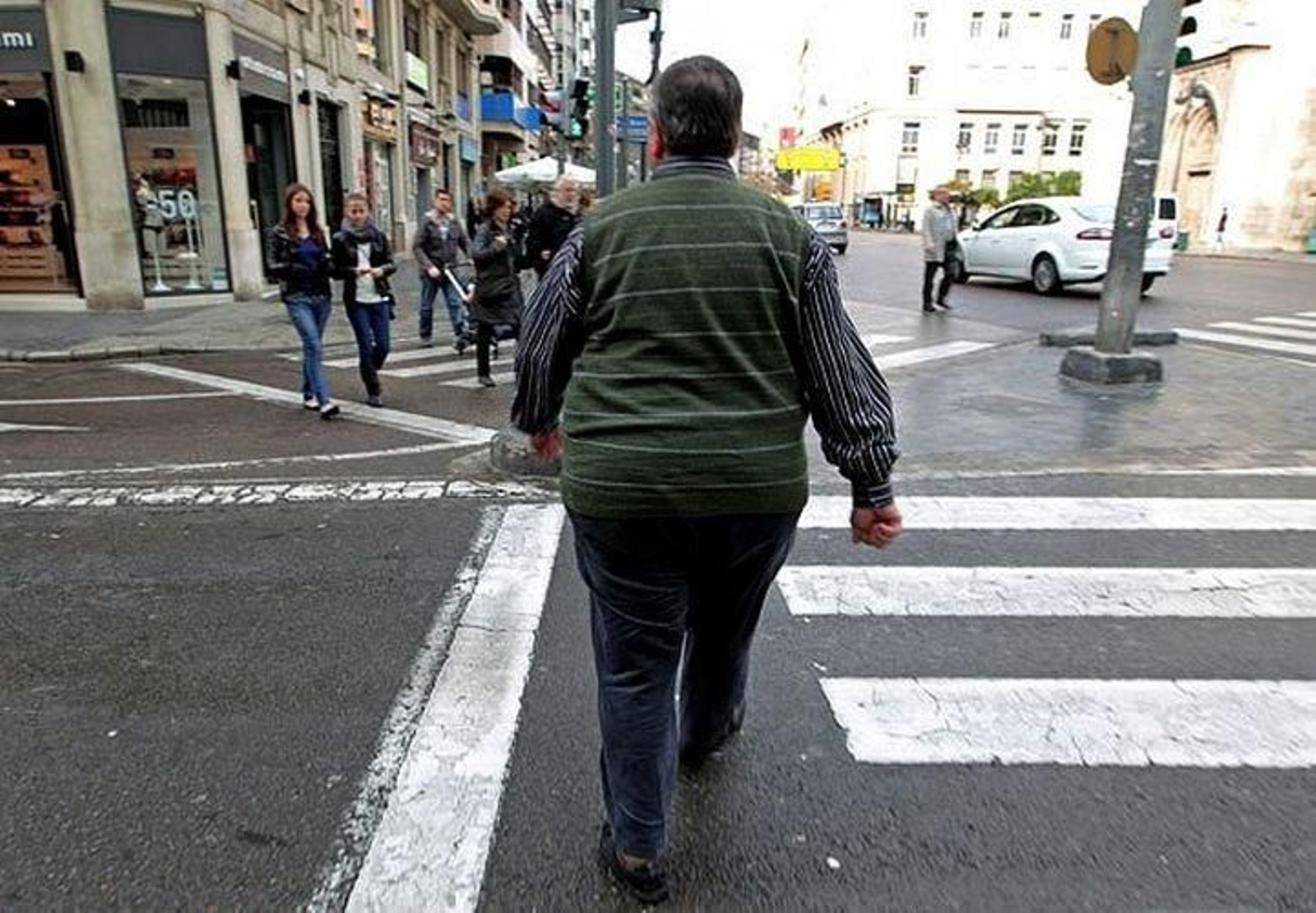 Un hombre obeso cruza un paso de peatones.