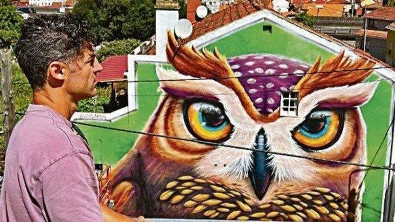 El artista vigués Pablo Loyola ante su mural “O moucho da vía” en la calle Robleda 118.