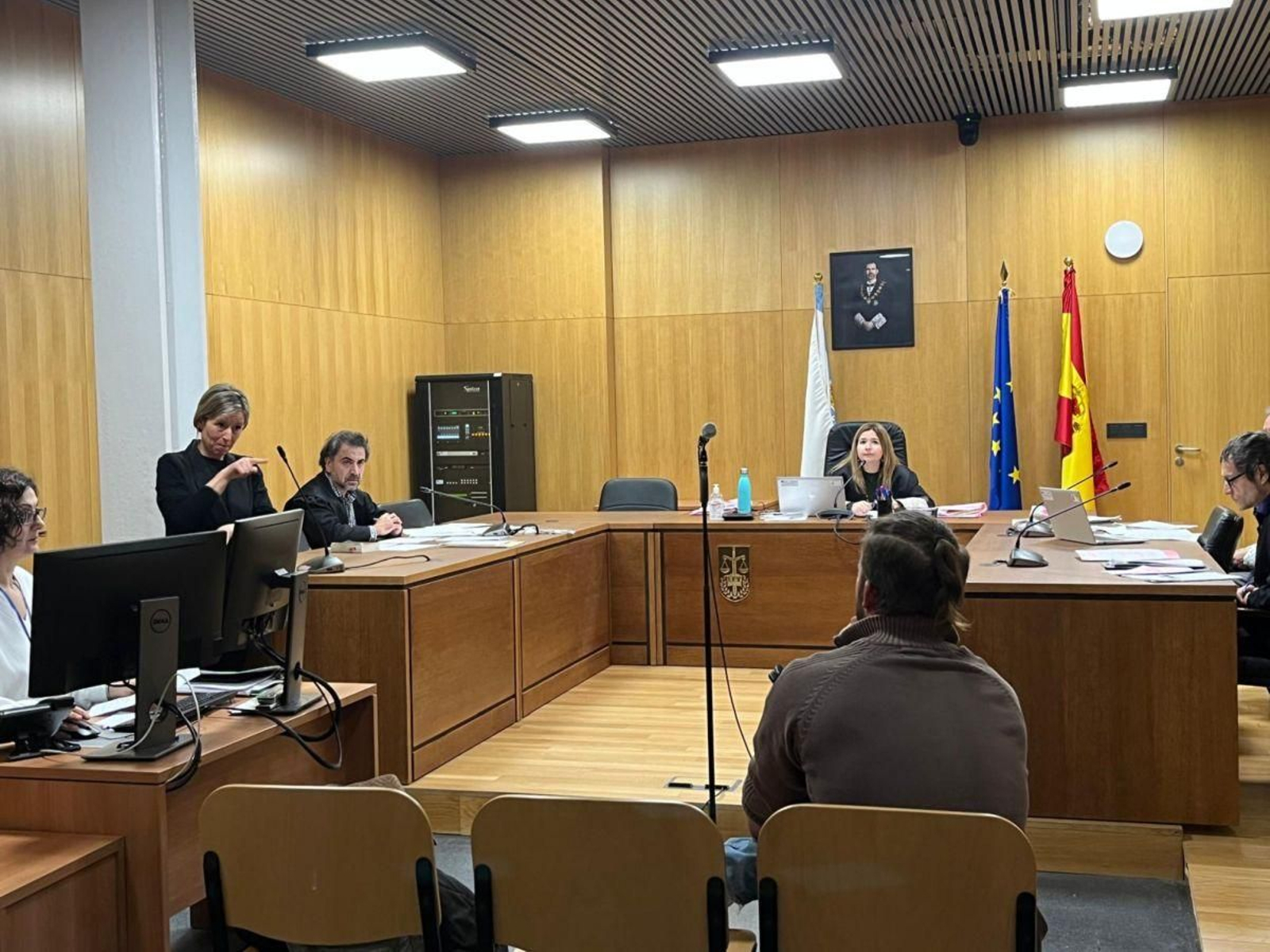 La intérprete de lengua de signos (en pie a la izquierda) traduce al acusado (sentado).