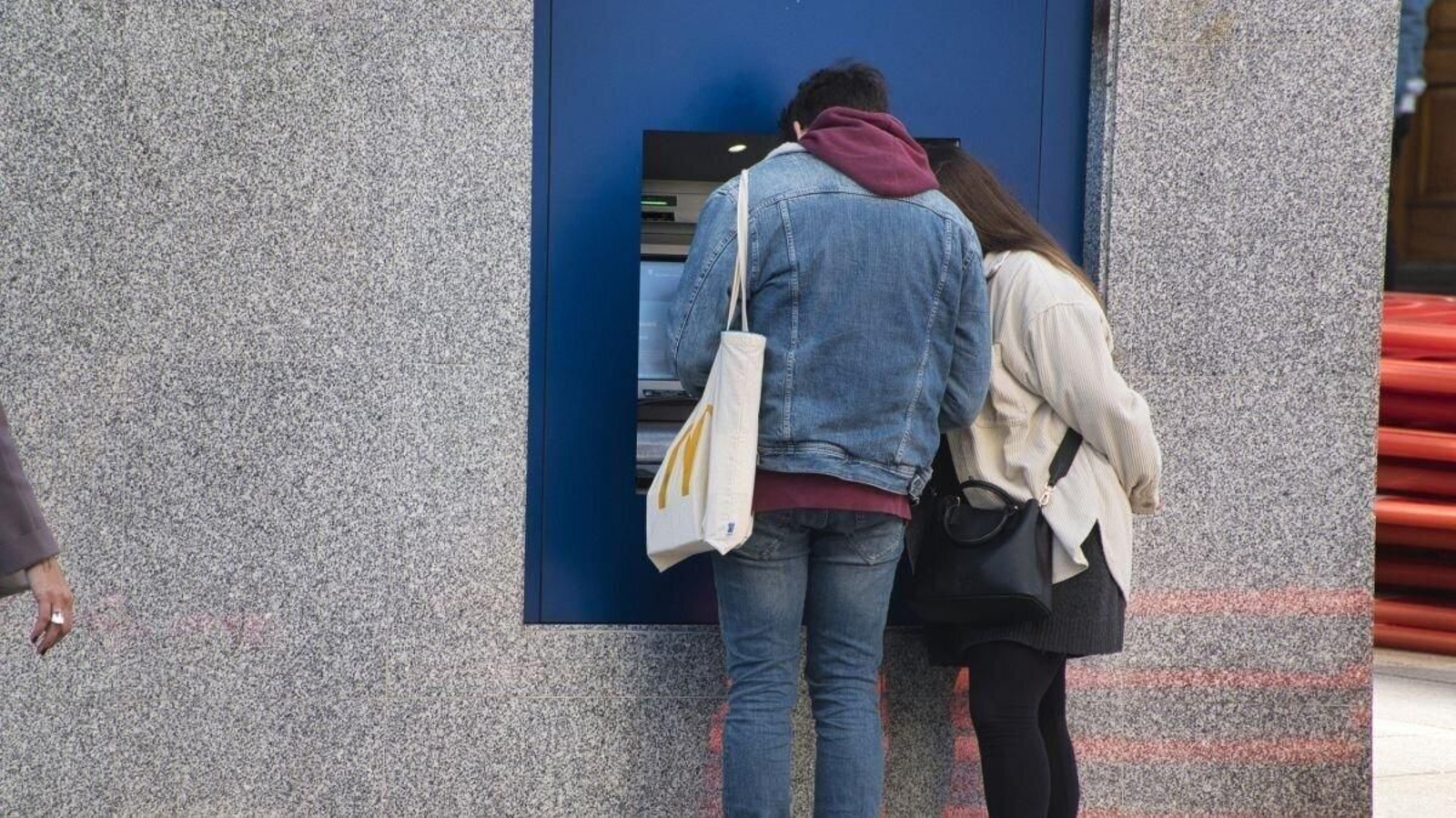 Dos personas sacan dinero de un cajero.