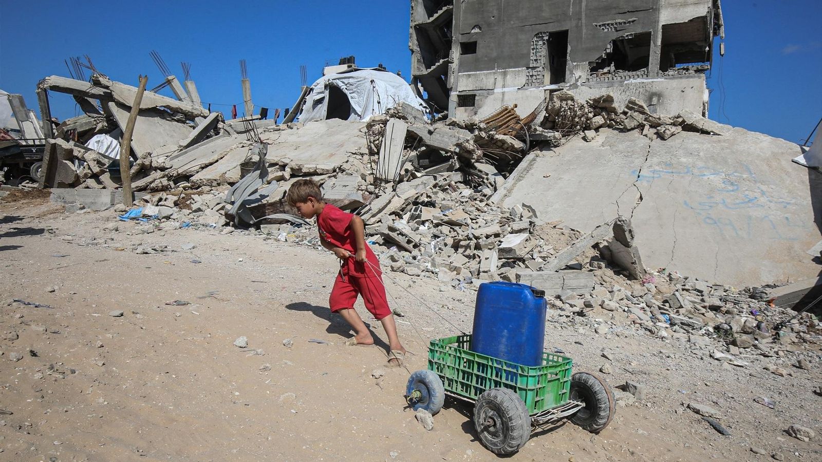 Un niño arrastra un bidón de agua en un carrito.