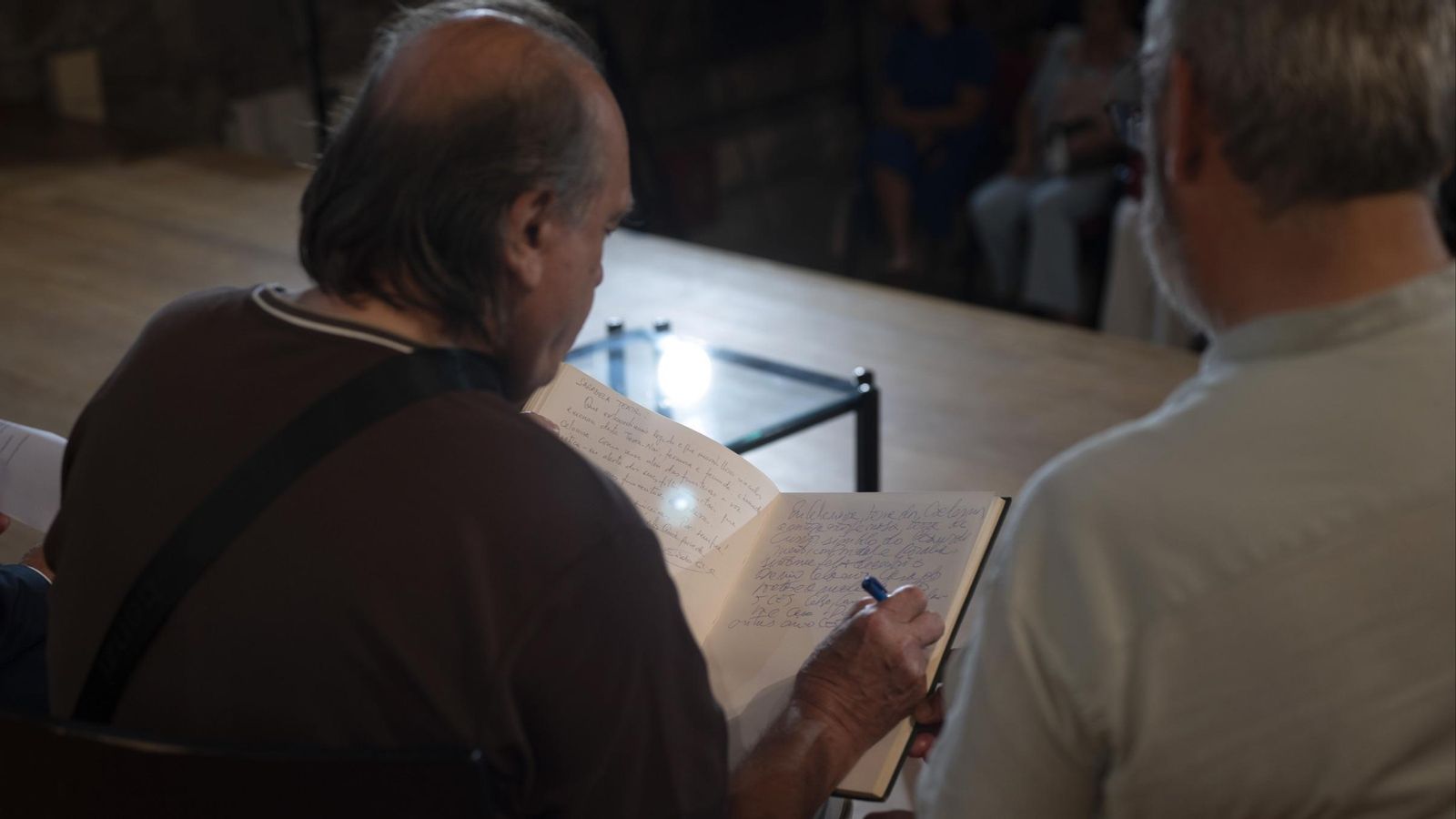 Xosé Lois González, escribindo lo libro de honra da Fundación Curros Enríquez acompañado por Antonio Piñeiro.