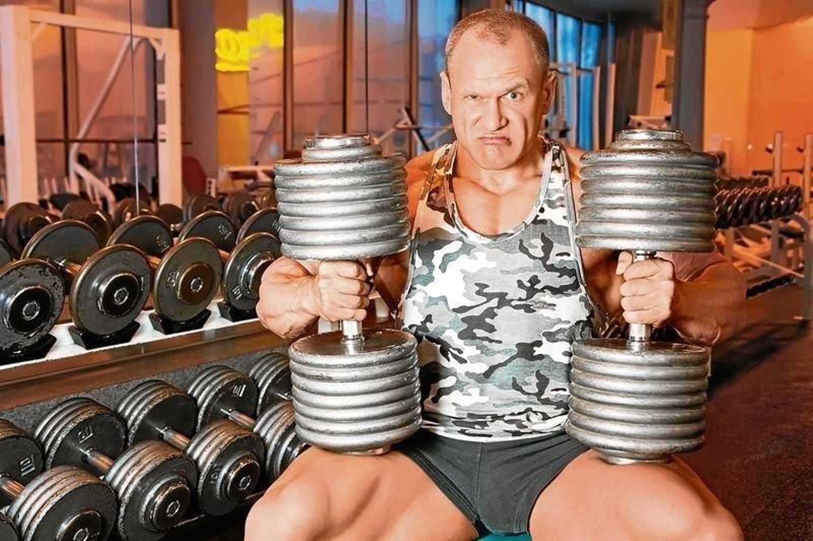 Un hombre muy musculado con dos mancuernas en sus manos.