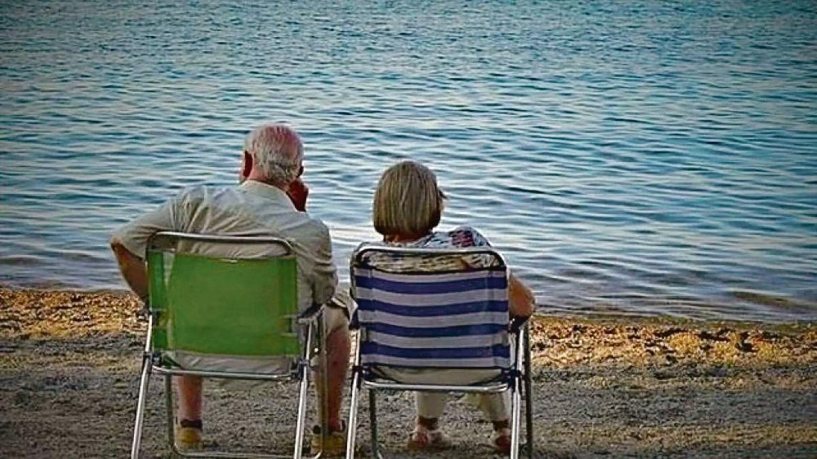Dos jubilados, sentados en una silla, obervan el mar.