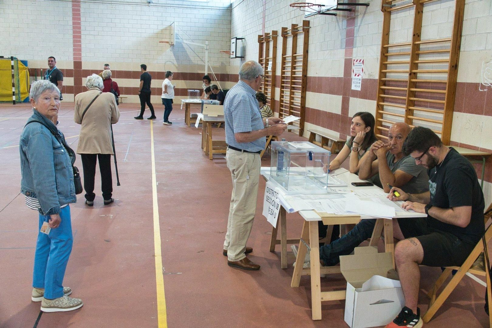 Un hombre muestra su DNI a los miembros de la mesa y procede a depositar su voto en la urna.
