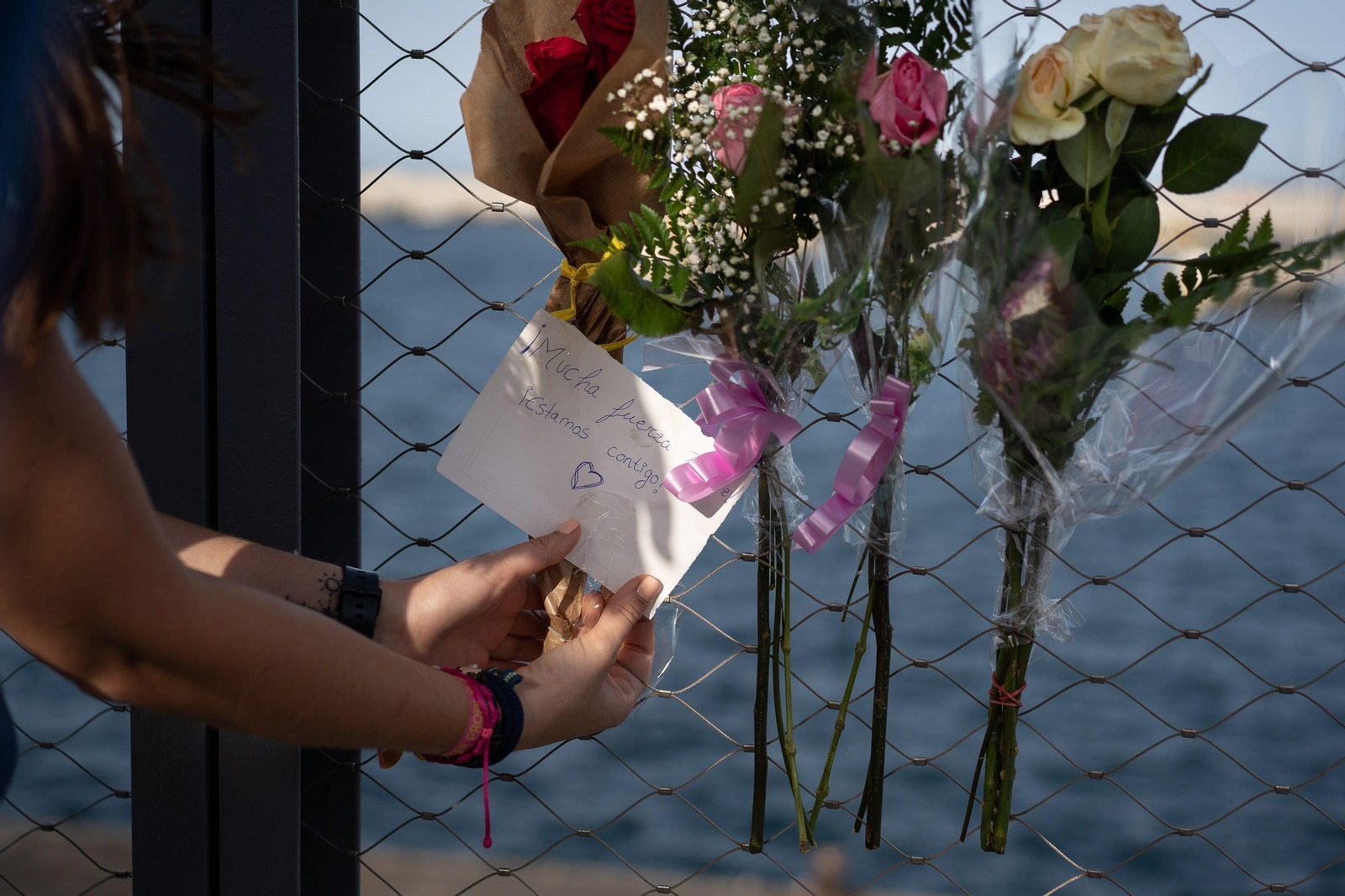 Una mujer coloca un ramo de flores en una valla del puerto de Santa Cruz de Tenerife.