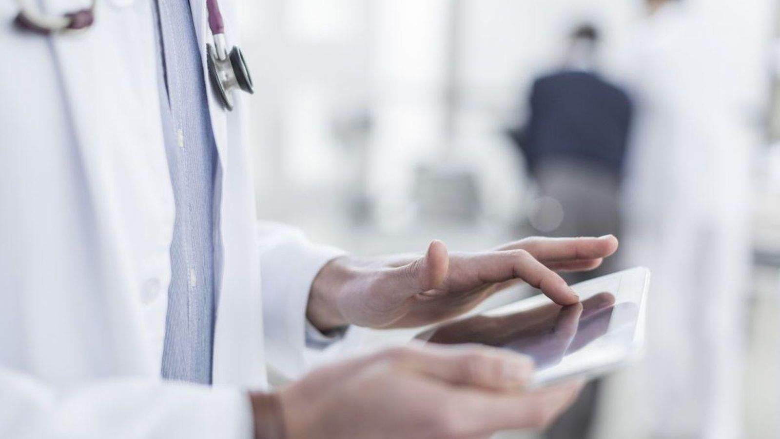 Un médico consulta un dispositivo móvil desde su puesto de trabajo.