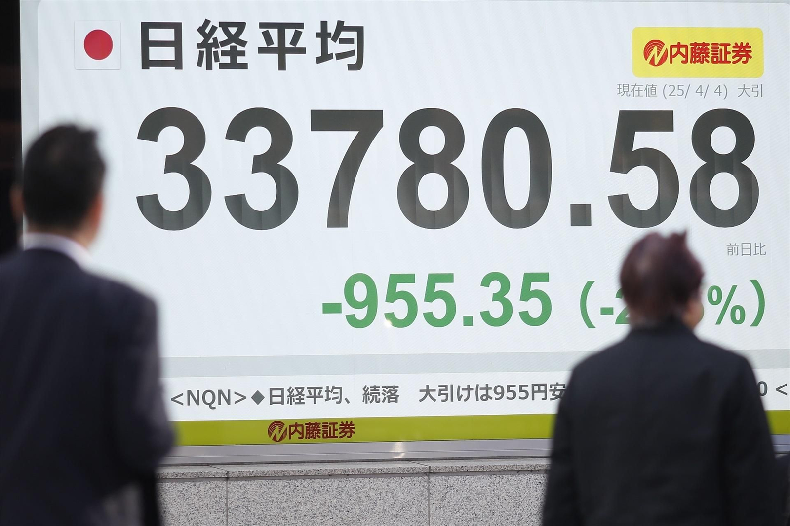Varias personas pasan junto a una pantalla electrónica que muestra el índice Nikkei japonés