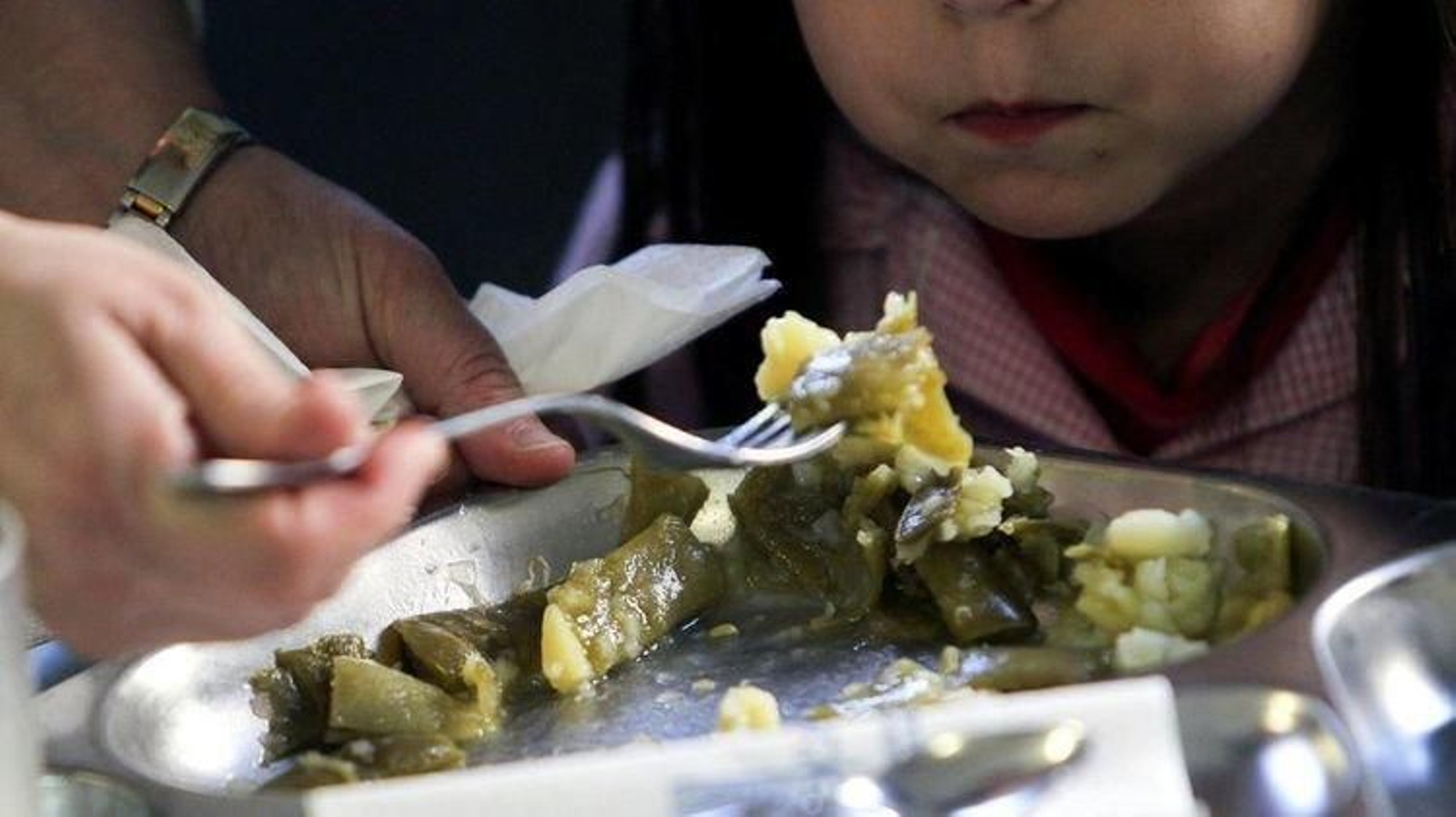 Una docente ayuda a una alumna en un comedor escolar.