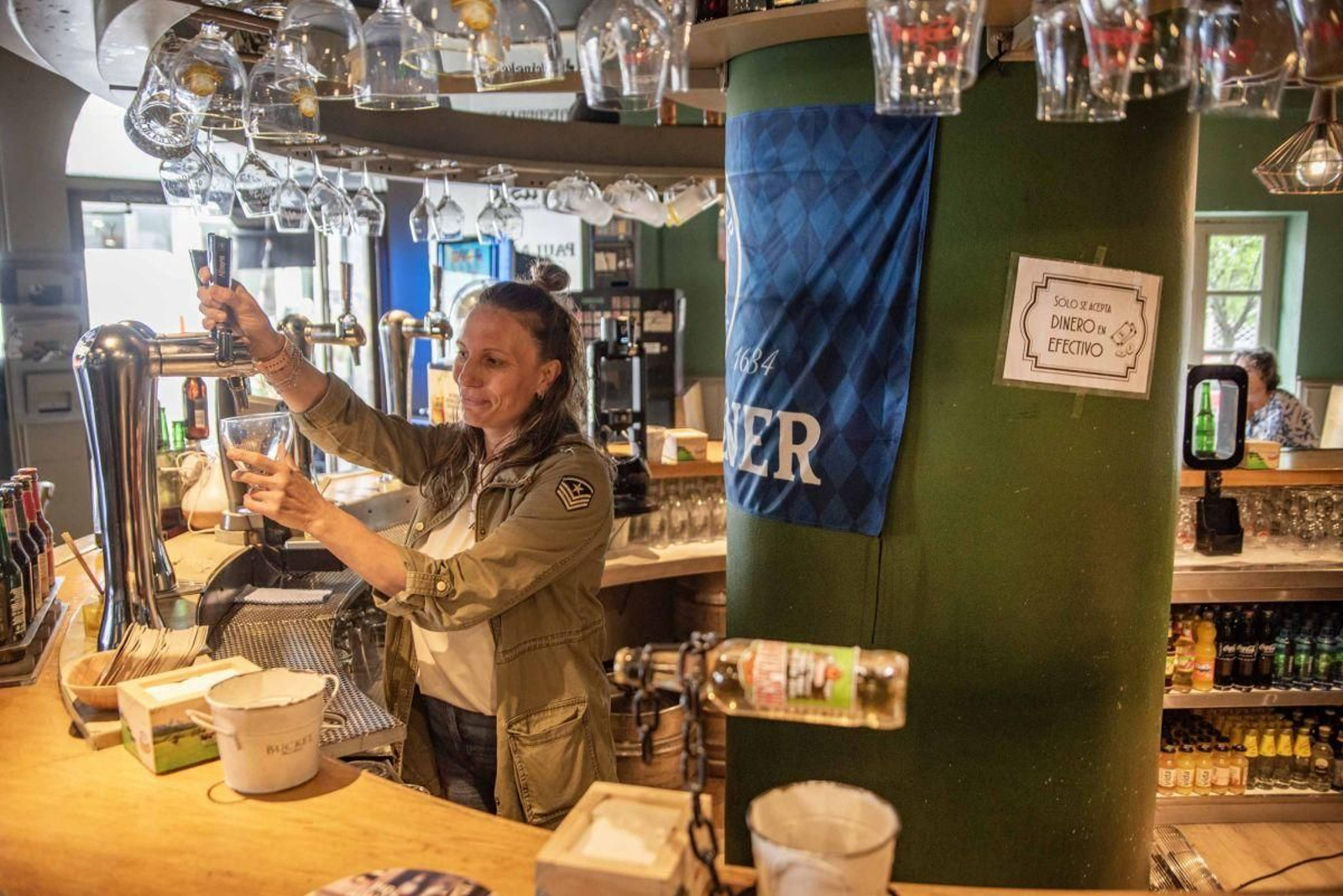 Verónica Domínguez, propietaria del la Cervecería Grifone, junto al cartel de: “Solo se acepta dinero en efectivo”.