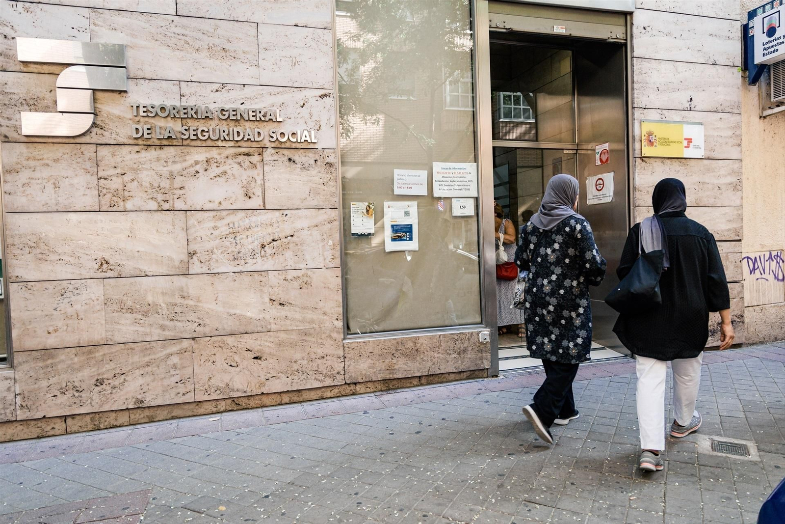 Varias personas migrantes esperan en el exterior de una oficina de la Seguridad Social.