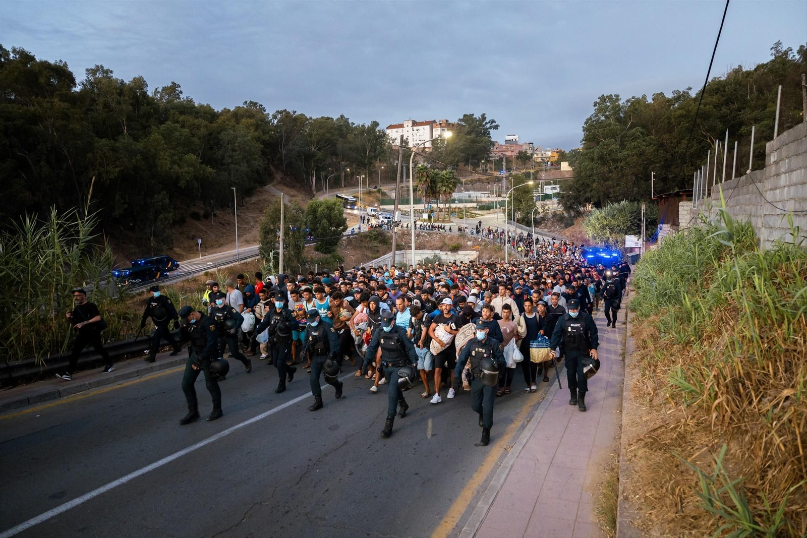 Centenares de personas se trasladan a pie durante el dispositivo de reubicación de migrantes hasta un nuevo centro temporal, en el barrio de Los Rosales.