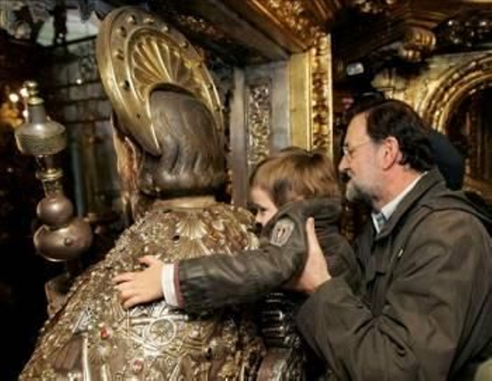 El presidente del PP, Mariano Rajoy, sostiene en brazos a su hijo mientras éste abraza la imagen del apóstol en la catedral de Santiago. (Foto: X. Rey)