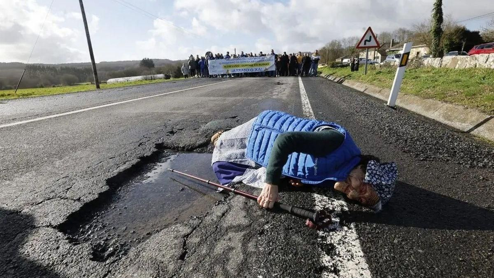 Una persona disfrazada tumbada al lado de un bache de la N-540, demostrando que algunos son tan grandes como una persona.