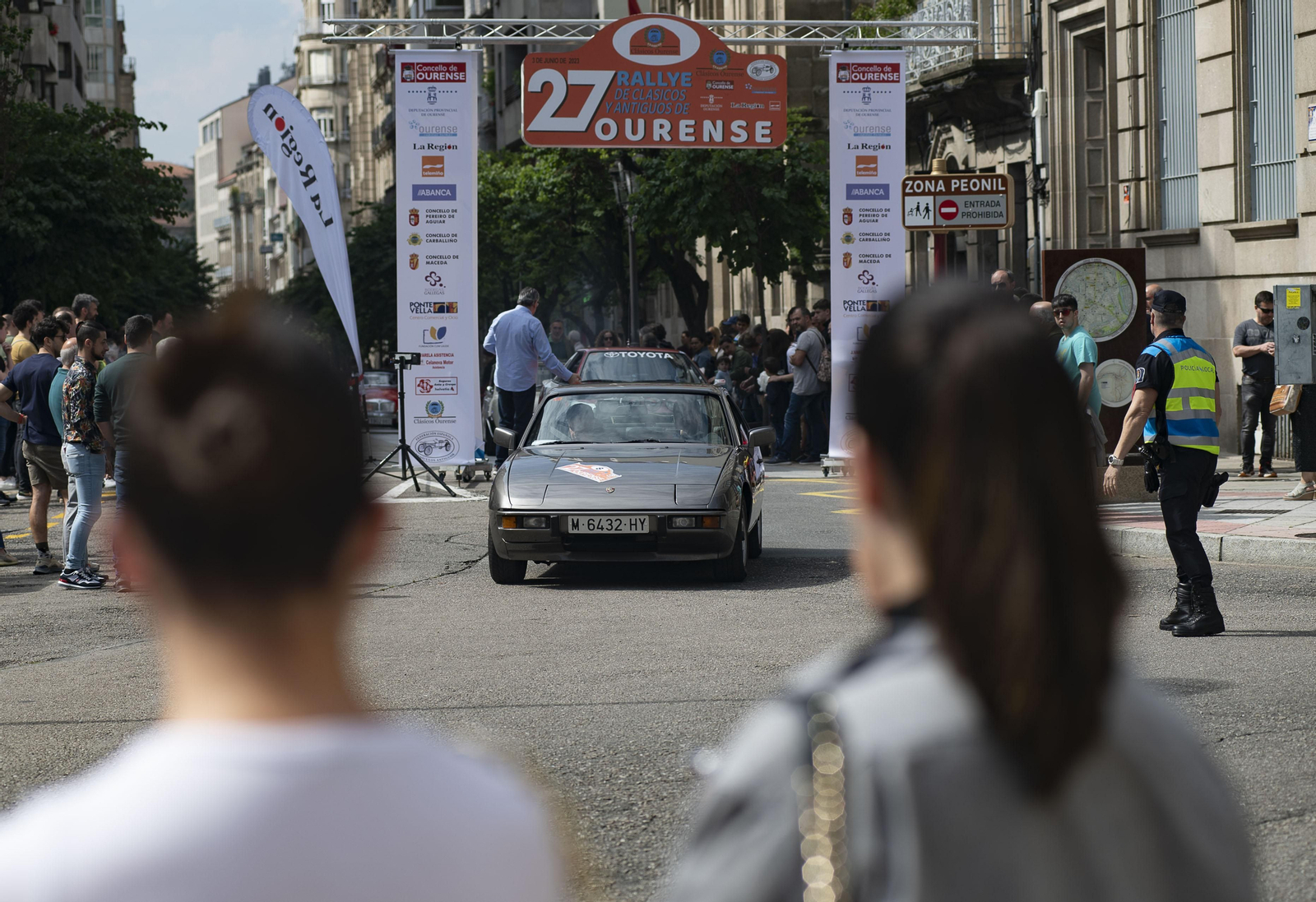 Personas observando pasar un coche de rally antiguo circulando por Ourense
