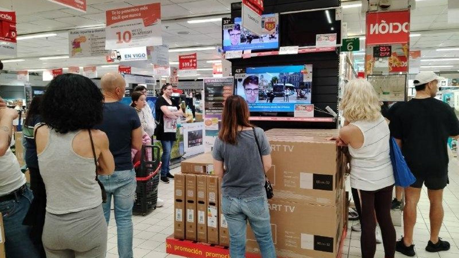 Gente siguiendo las noticias en los televisores de un supermercado.